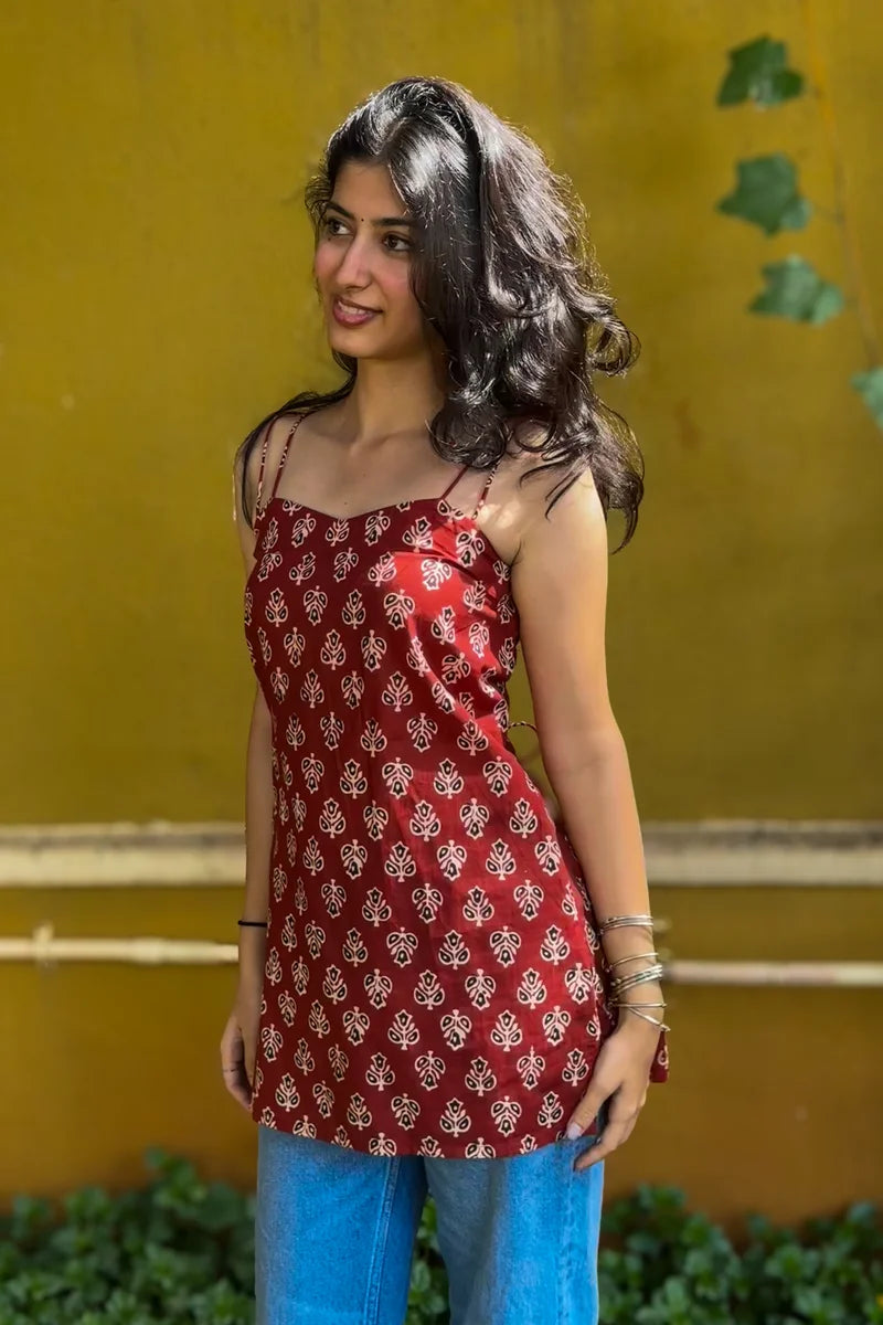 Woman wearing a butta red patterned top and pants against a wall.