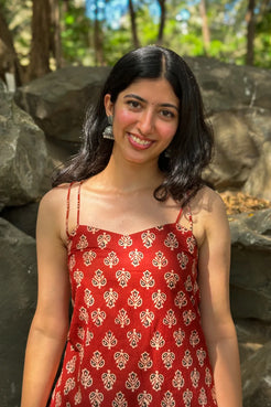 Woman wearing a butta red dress with patterns standing outdoors with rocks and greenery in the background