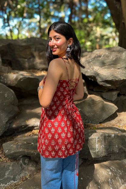 Woman in a butta red patterned top and jeans standing in a natural setting with rocks and trees.