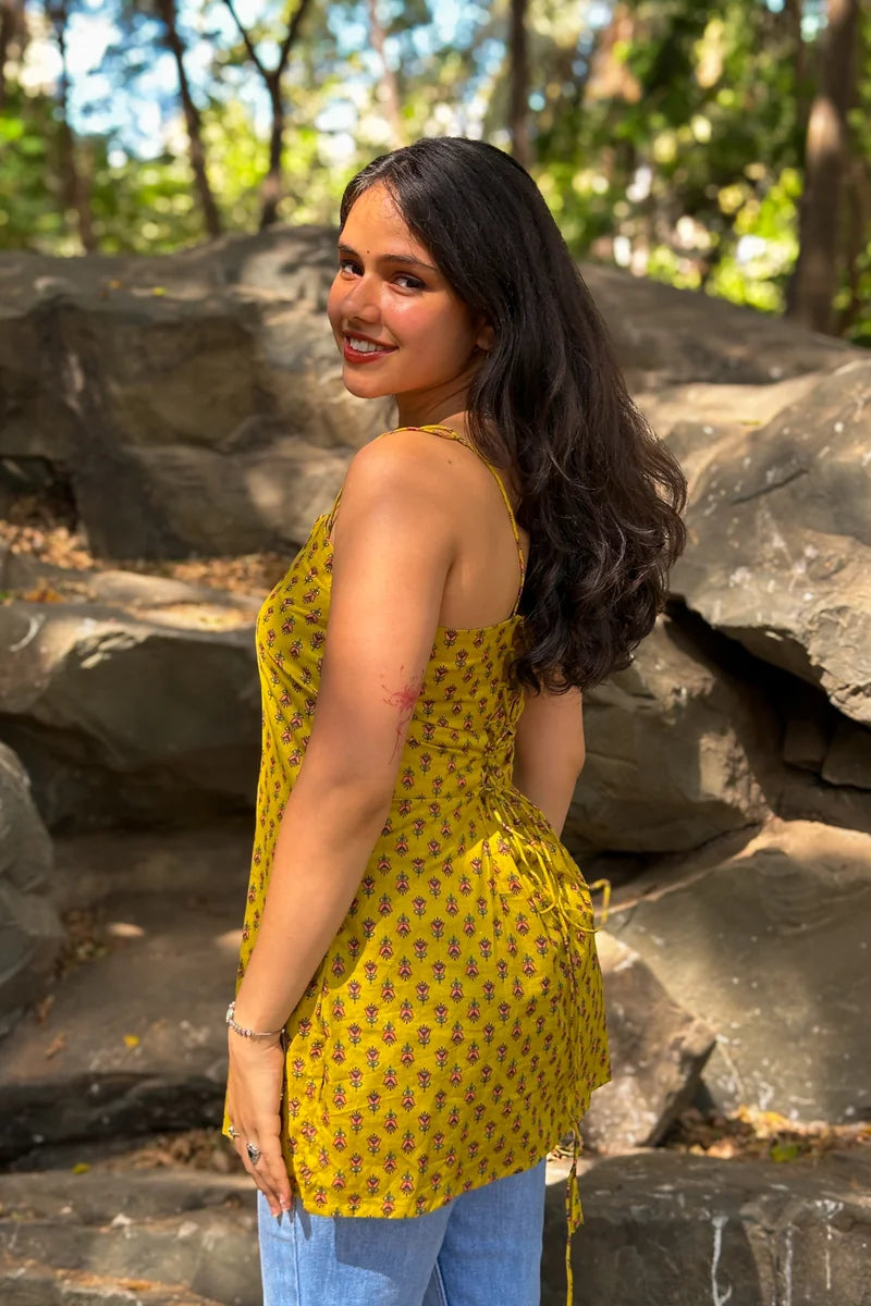Woman in a jiva-yellow top with floral patterns standing in a natural setting with rocks and trees.