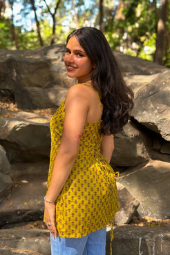 Woman in a jiva-yellow top with floral patterns standing in a natural setting with rocks and trees.