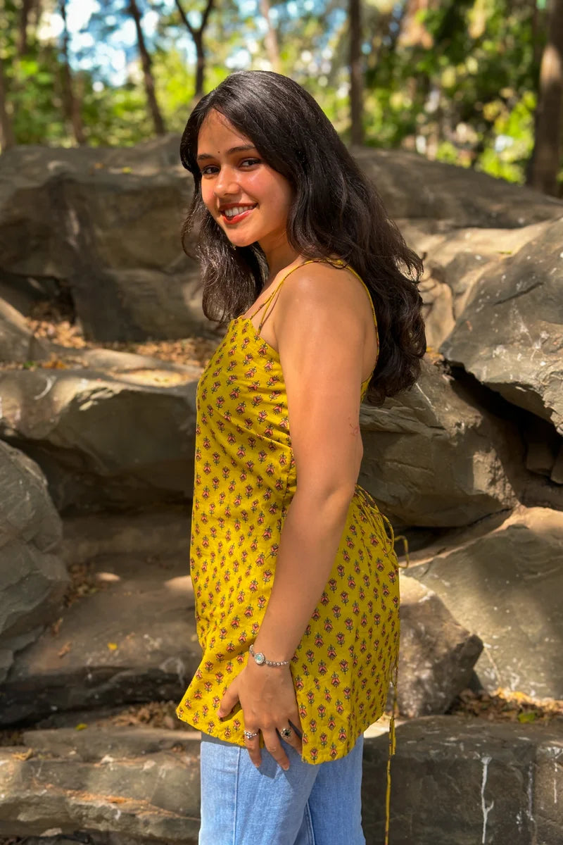 Woman in a jiva-yellow dress standing among rocks with trees in the background