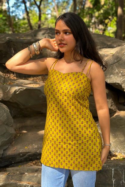 Woman wearing a jiva-yellow patterned top and blue jeans standing outdoors with rocks and greenery in the background