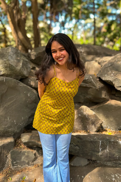 Woman in a jiva-yellow top and blue jeans standing in front of large rocks with trees in the background