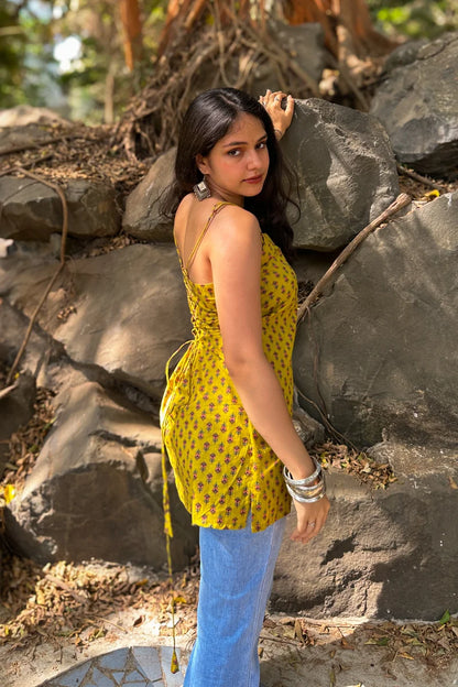 Woman in a jiva-yellow patterned top and blue jeans standing against rocks outdoors