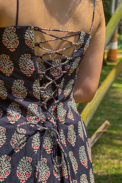 Person wearing a paisley dress with a pattern of red and green leaves, standing outdoors.