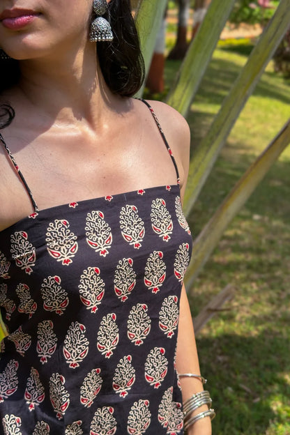 Person wearing a paisley black dress with a pattern, standing outdoors with greenery in the background