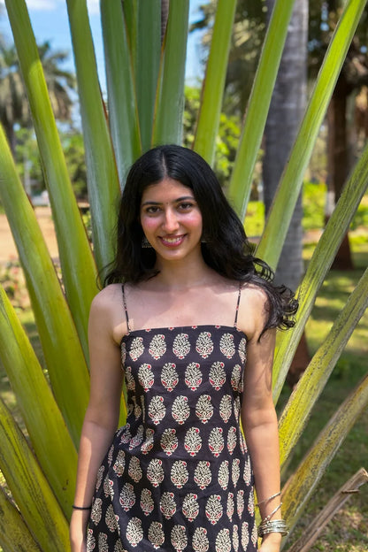 Woman in a paisley black patterned dress standing among palm leaves