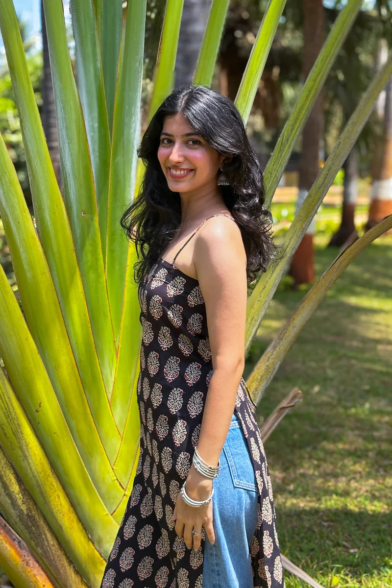 Woman in a paisley patterned dress standing among large green leaves in a park.