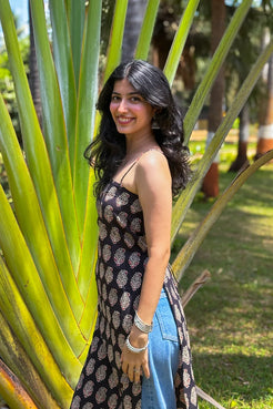 Woman in a paisley patterned dress standing among large green leaves in a park.