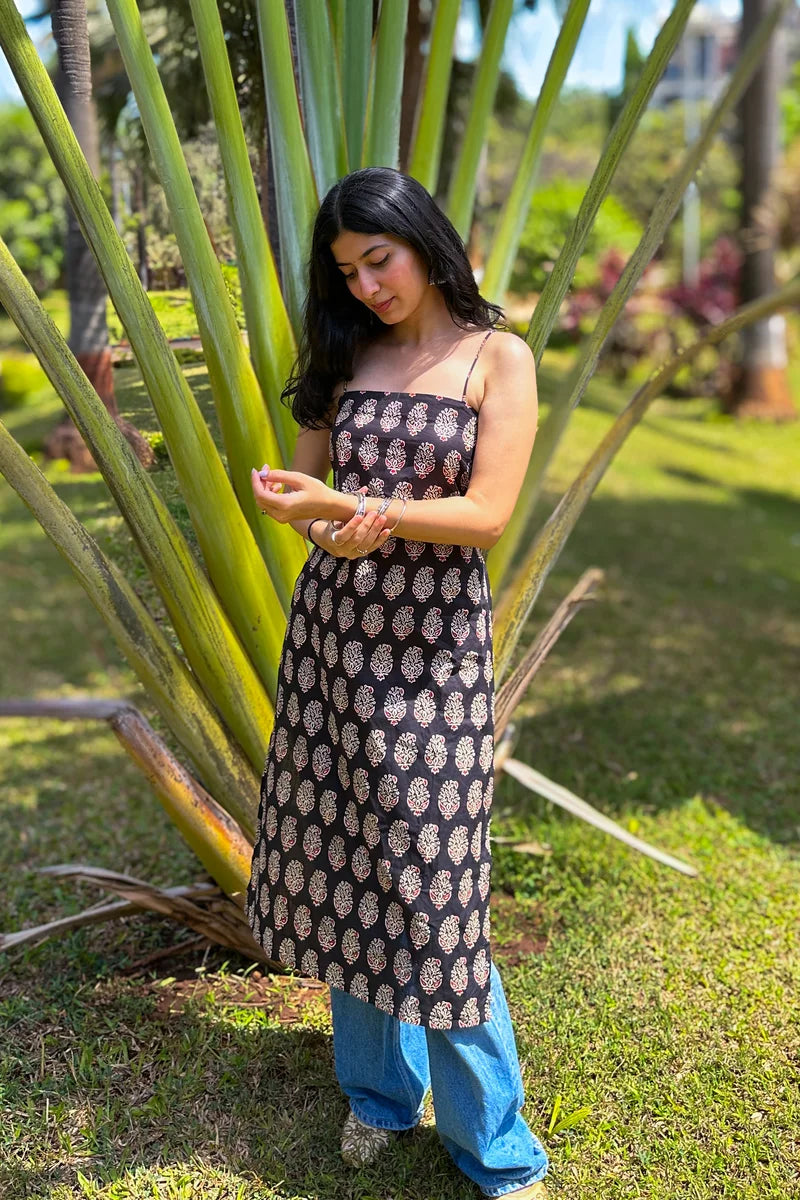 Woman in a paisley patterned dress standing next to a tall plant in a garden