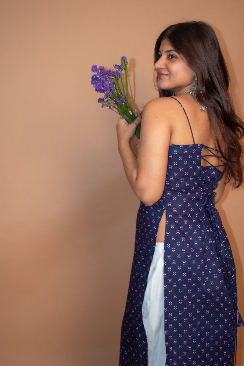 Woman in a jiva-blue dress holding purple flowers against a beige background