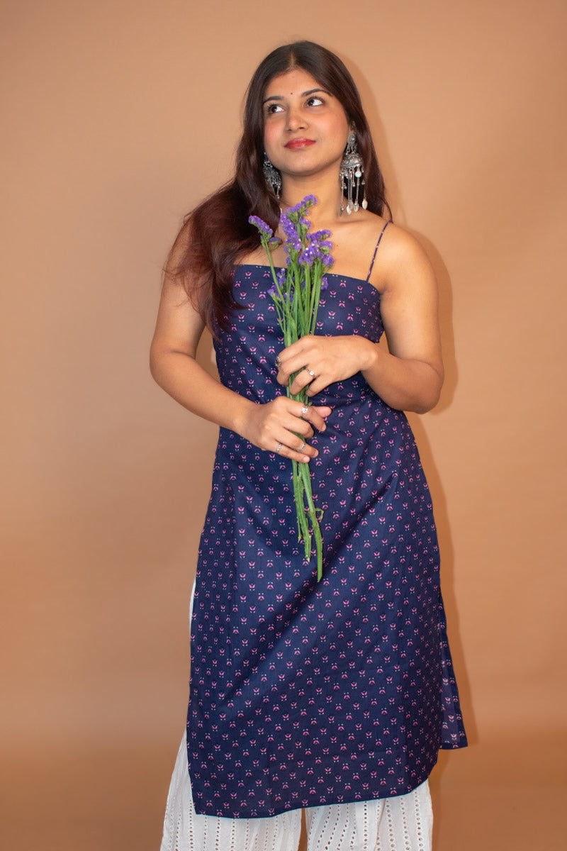 Woman wearing a jiva-blue patterned dress holding purple flowers against a beige background