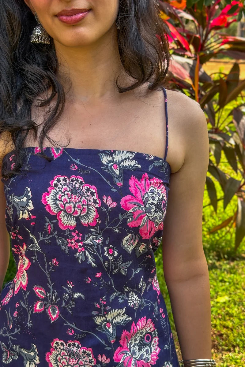 Woman wearing a jal-blue floral dress with pink and white flowers against a natural background