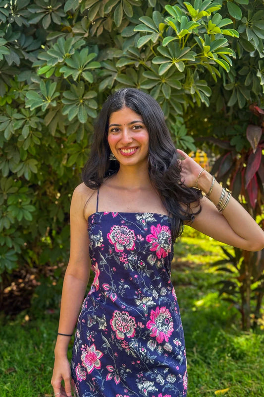 Woman in a jal-blue floral dress standing in front of green foliage