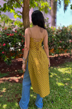 Person wearing a jiva-yellow patterned dress and blue jeans standing in a garden.