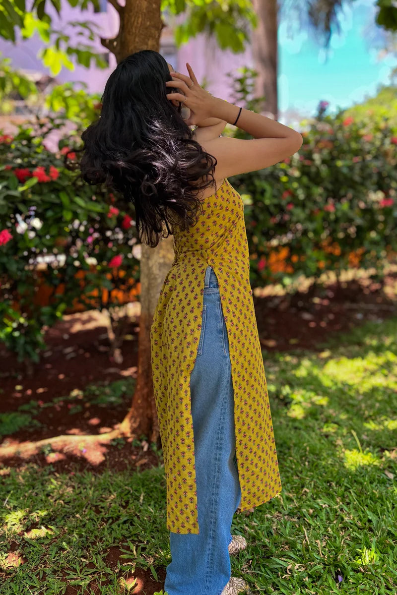 Woman in a jiva-yellow patterned top and blue jeans standing in a garden.
