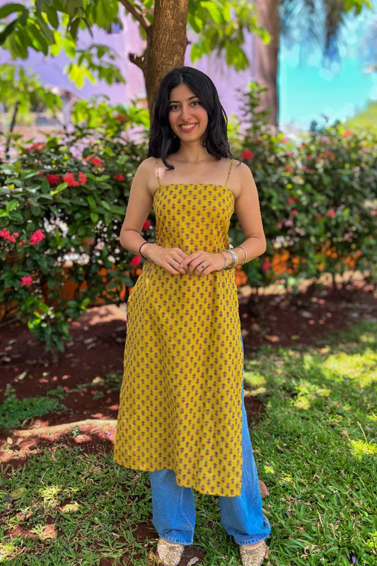 Woman in a jiva-yellow dress with a floral pattern standing in a garden.