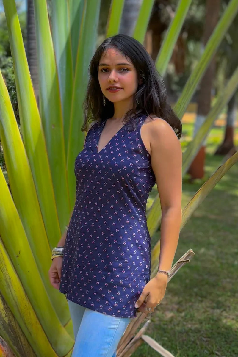 Woman in a jiva-blue patterned top standing among tall green plants