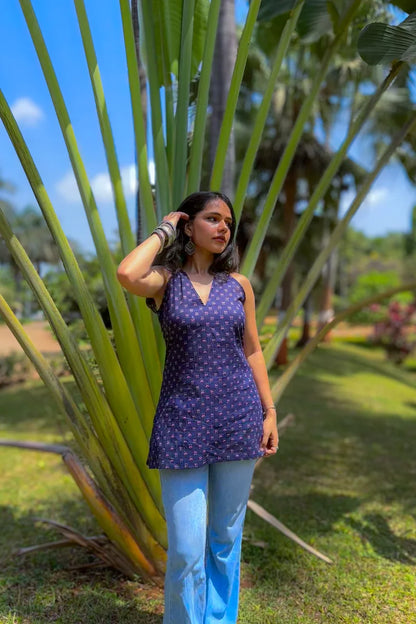 Woman in a jiva-blue dress standing in a garden with tall plants and blue sky.
