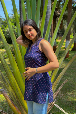 Woman in a jiva-blue patterned dress standing among tall green plants