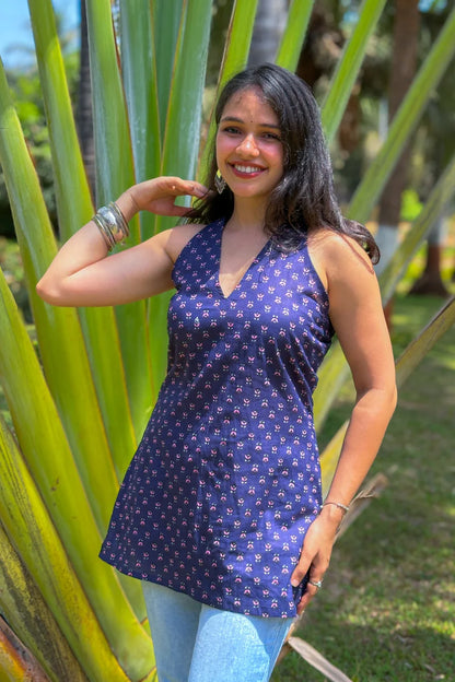 Woman wearing a jiva-blue patterned dress standing among tall green plants.