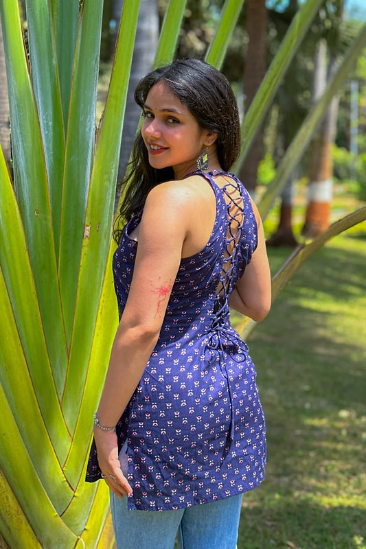 Woman in a jiva-blue dress standing among large green leaves outdoors