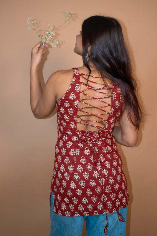 Woman wearing a butta red floral top with a unique back design against a beige background