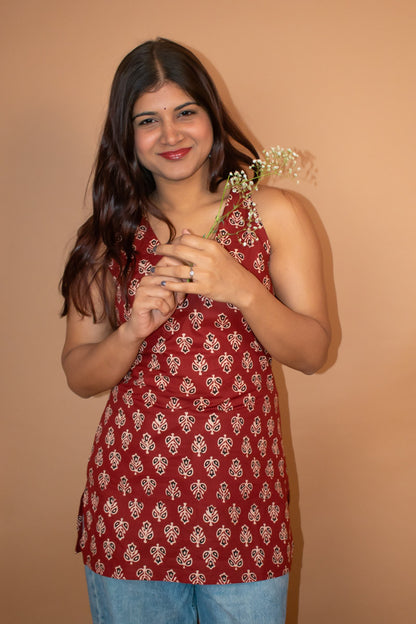 Woman wearing a butta red patterned top and blue jeans against a beige background