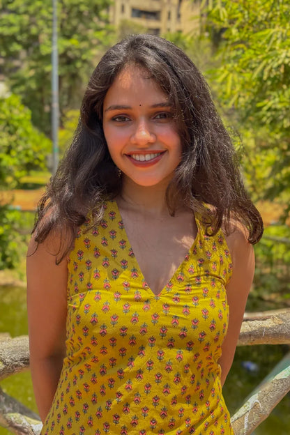 Woman in a jiva-yellow floral dress standing outdoors with greenery in the background
