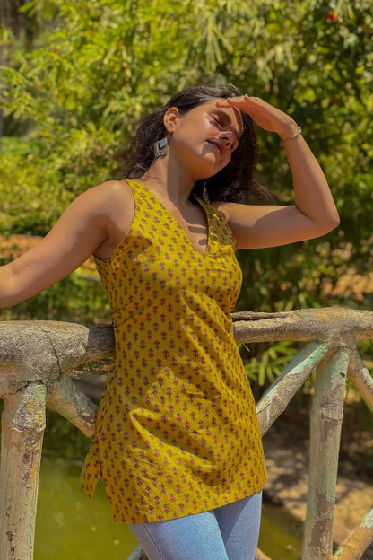Woman wearing a jiva-yellow patterned top standing outdoors with greenery in the background