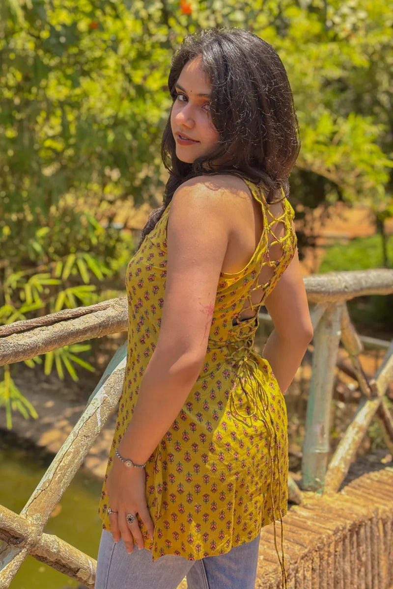 Woman in a jiva-yellow dress standing on a wooden bridge with greenery in the background