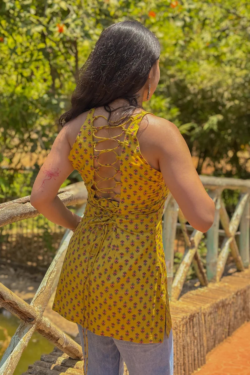 Woman wearing a jiva-yellow patterned top with a back design, standing outdoors.