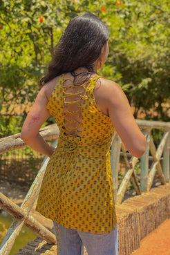 Woman wearing a jiva-yellow patterned top with a back design, standing outdoors.